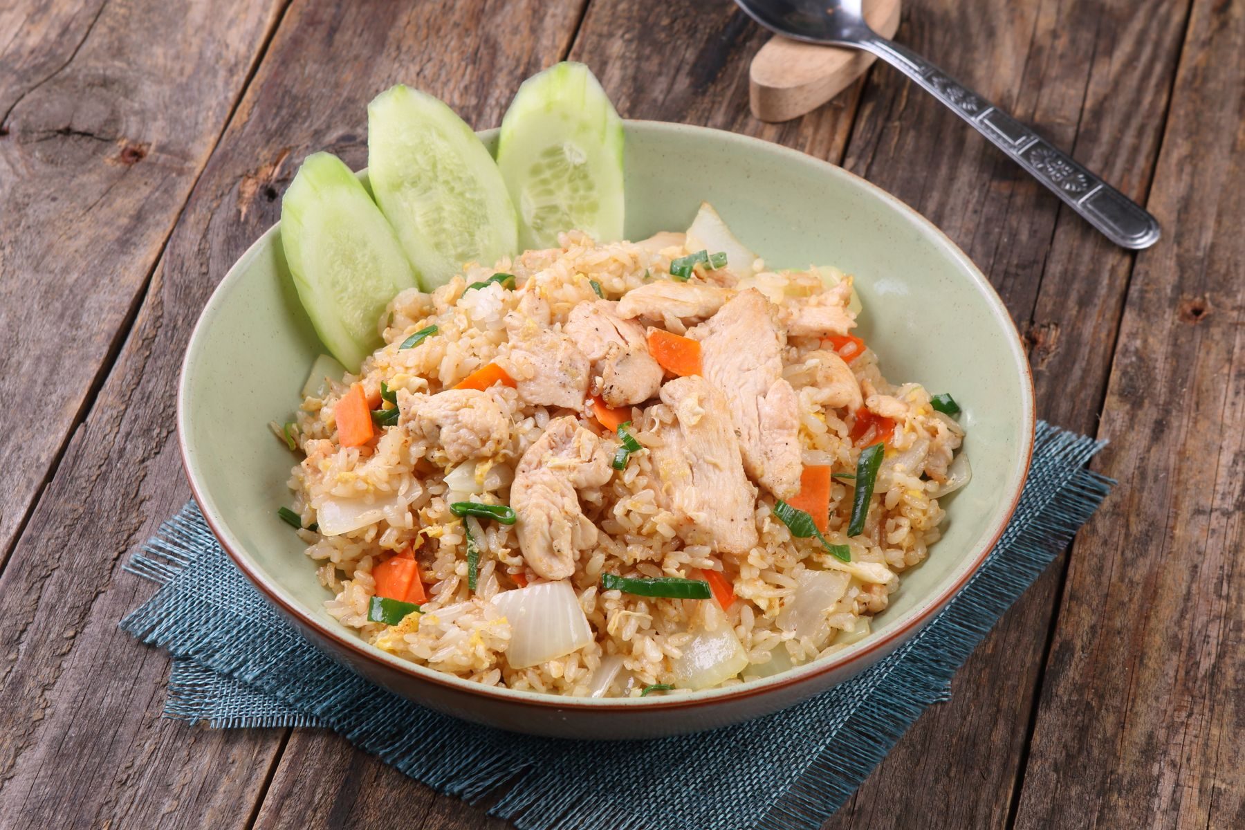 A bowl of fried rice with chicken, carrot and scallion, sliced cucumber on the rim