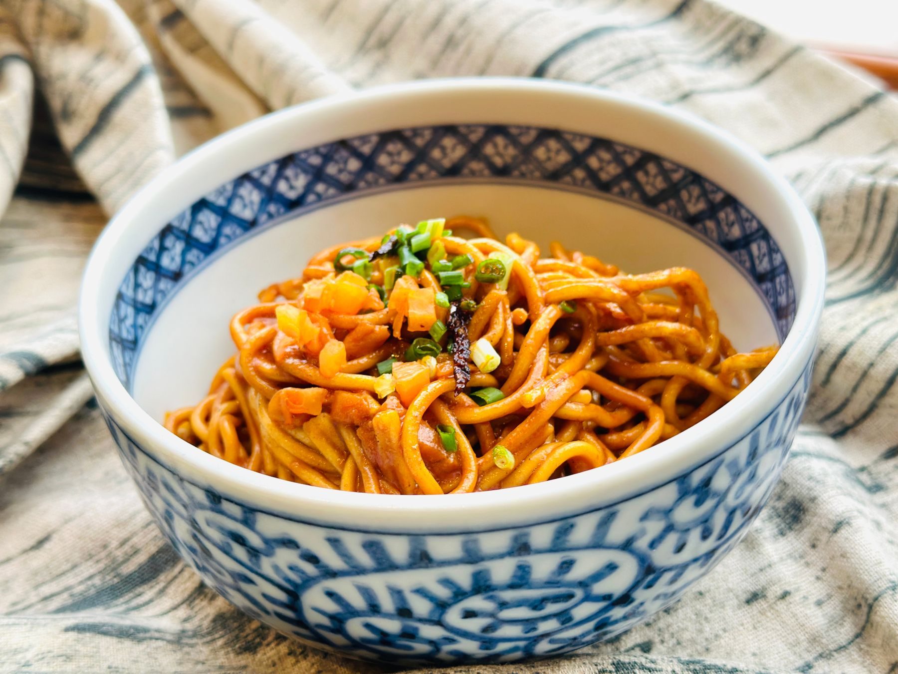 Noodles tossed glossy with scallions in a blue-and-white bowl — the late bowl