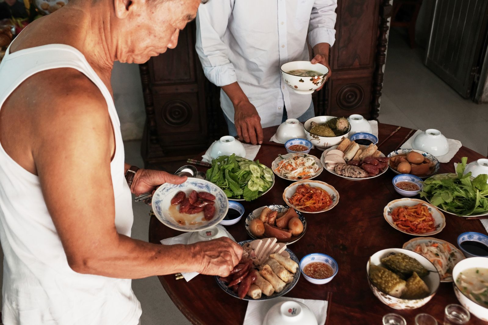 A Vietnamese family laying out the table at home, a dipping bowl beside every dish